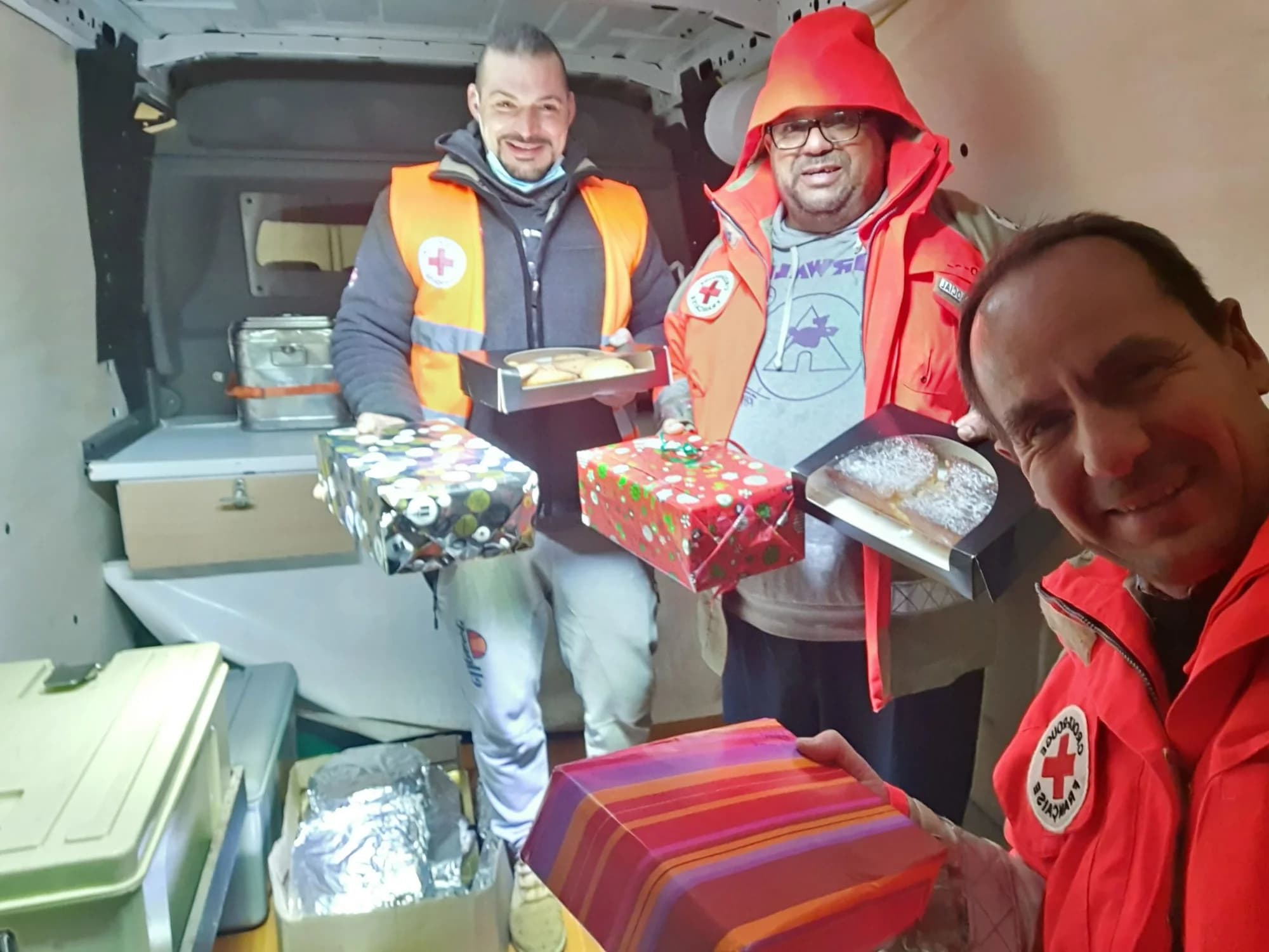 Trois bénévoles, dont deux de la Croix-Rouge, tiennent des boîtes emballées à l'arrière d'un camion.