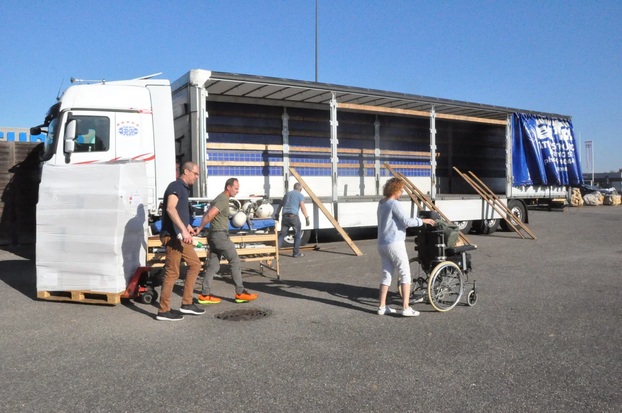 Des bénévoles chargent un lit médicalisé et un fauteuil roulant dans la remorque d'un semi-remorque.